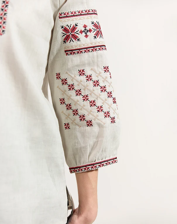 The sleeve of a linen shirt embroidered in red, black and beige cross-stitch, with geometric flower and diamond patterns