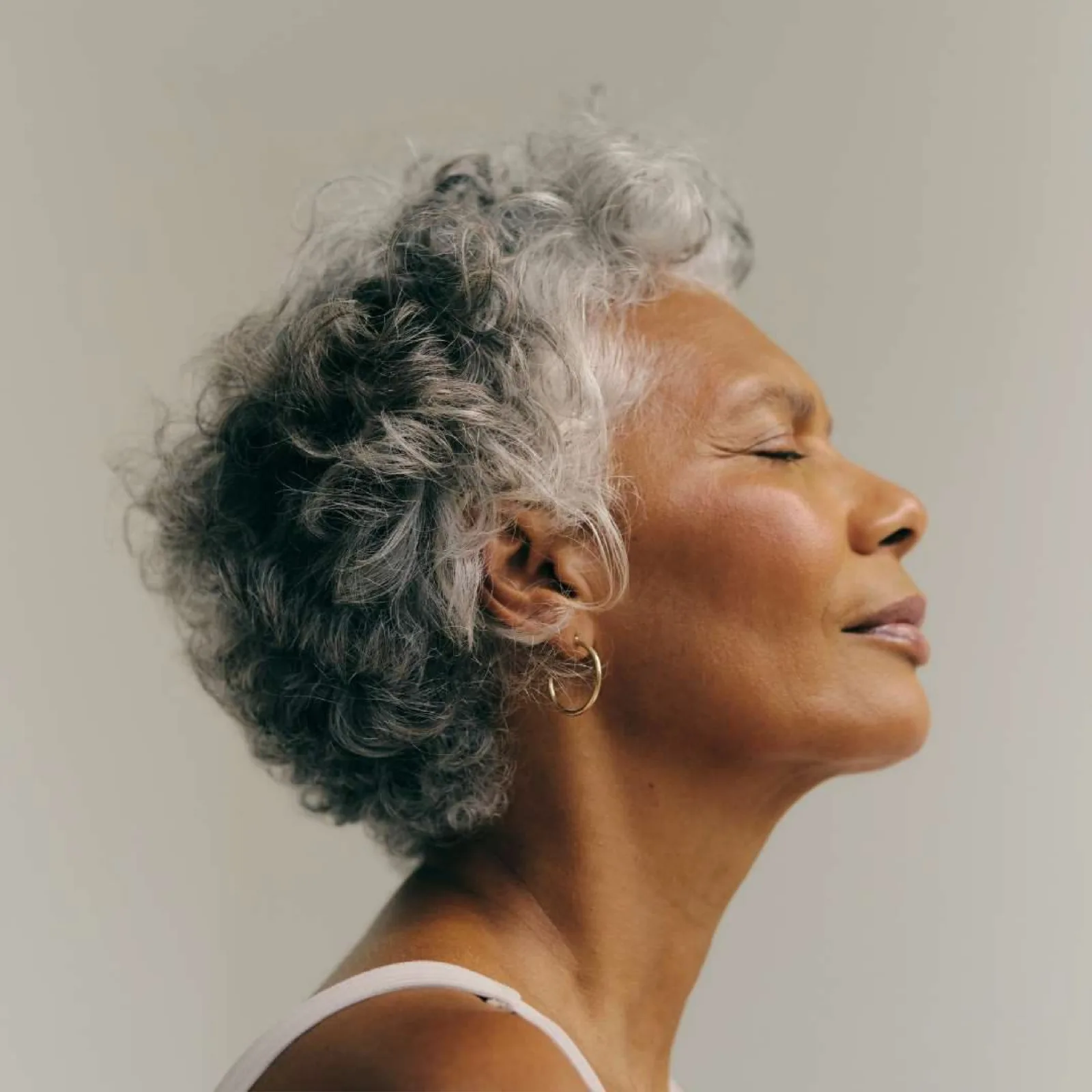 Portrait of a woman with silver curly hair in profile, eyes closed, face lifted to soft light