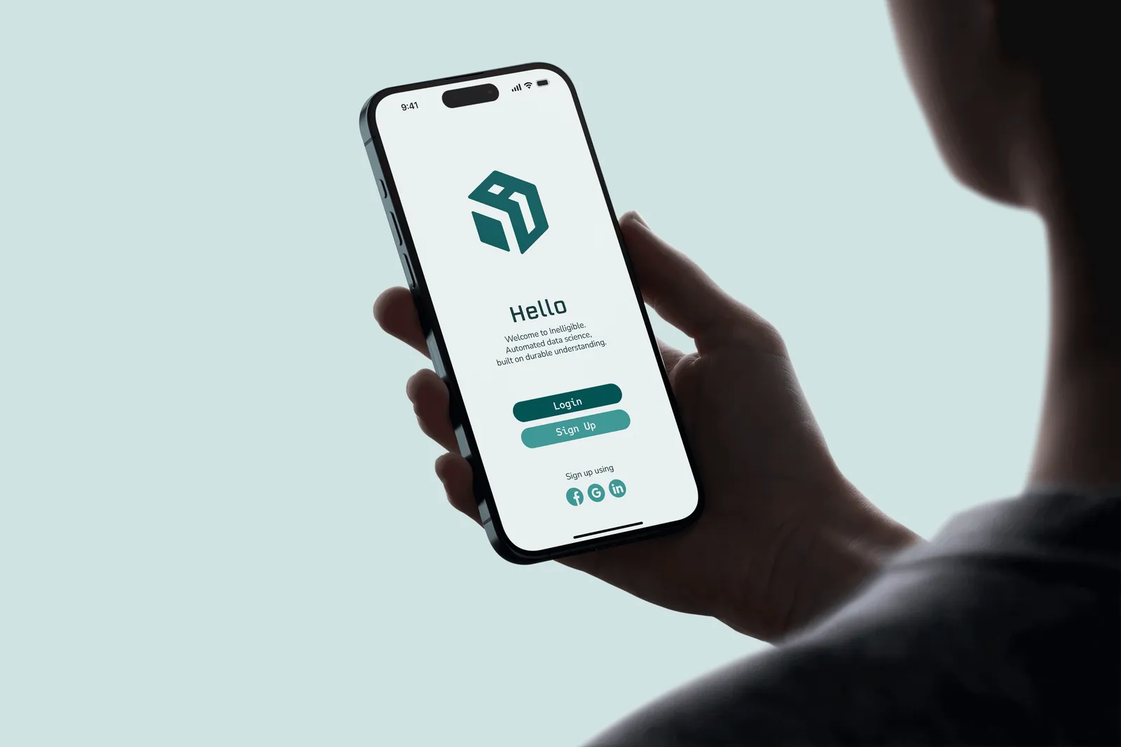 A phone held in hand, showing the Intelligible app's welcome screen with the cube icon and a Hello greeting