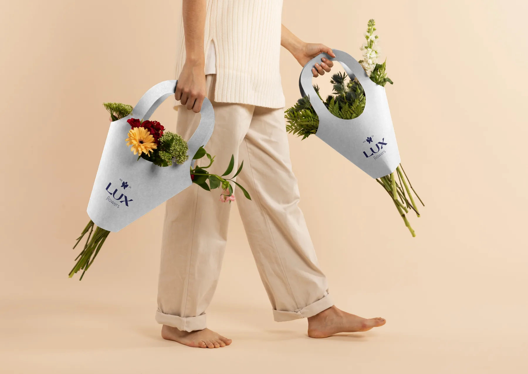 Someone carrying two bouquets in Lux Flowers branded paper carriers