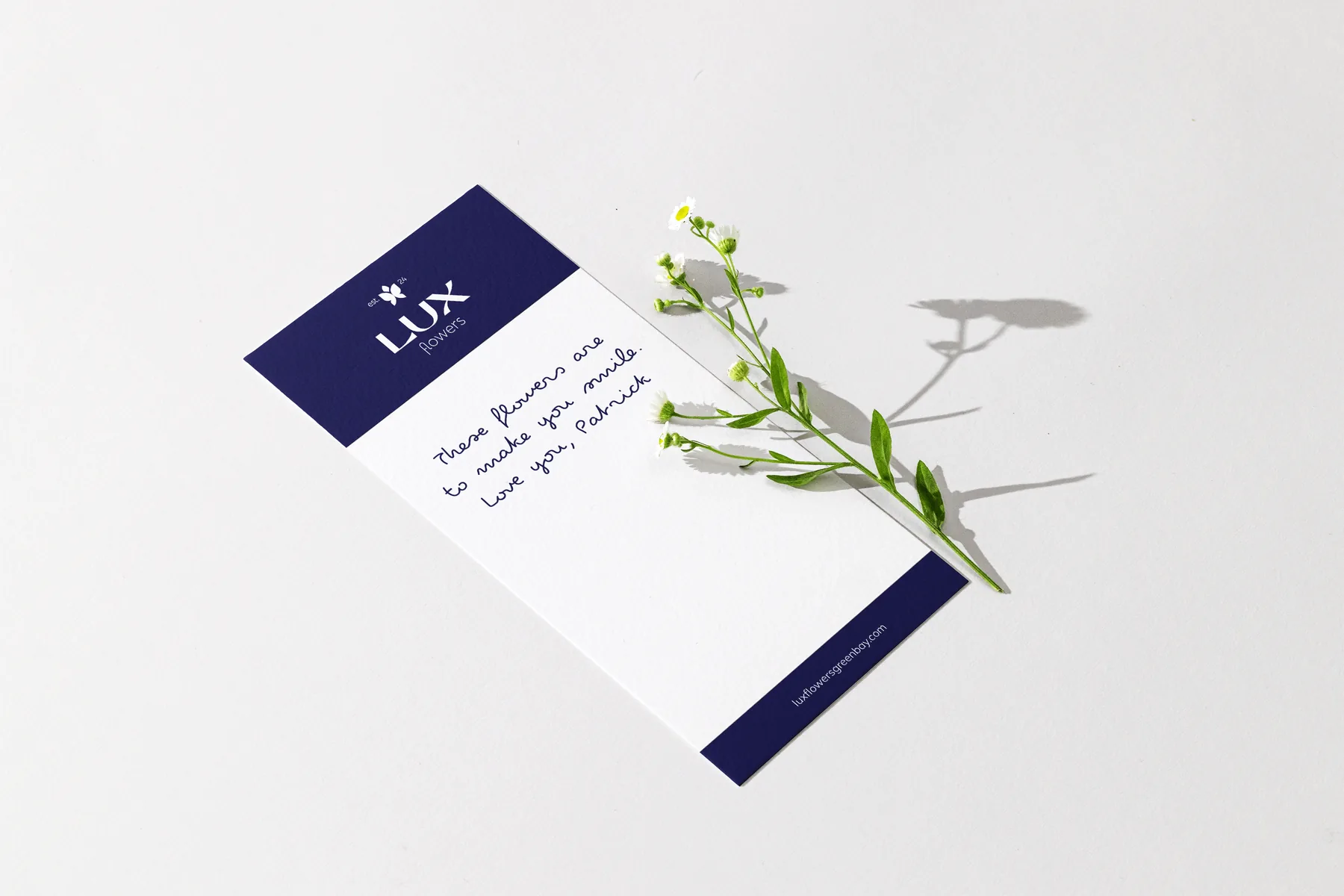 A Lux Flowers gift card with a handwritten note, beside a sprig of small white flowers