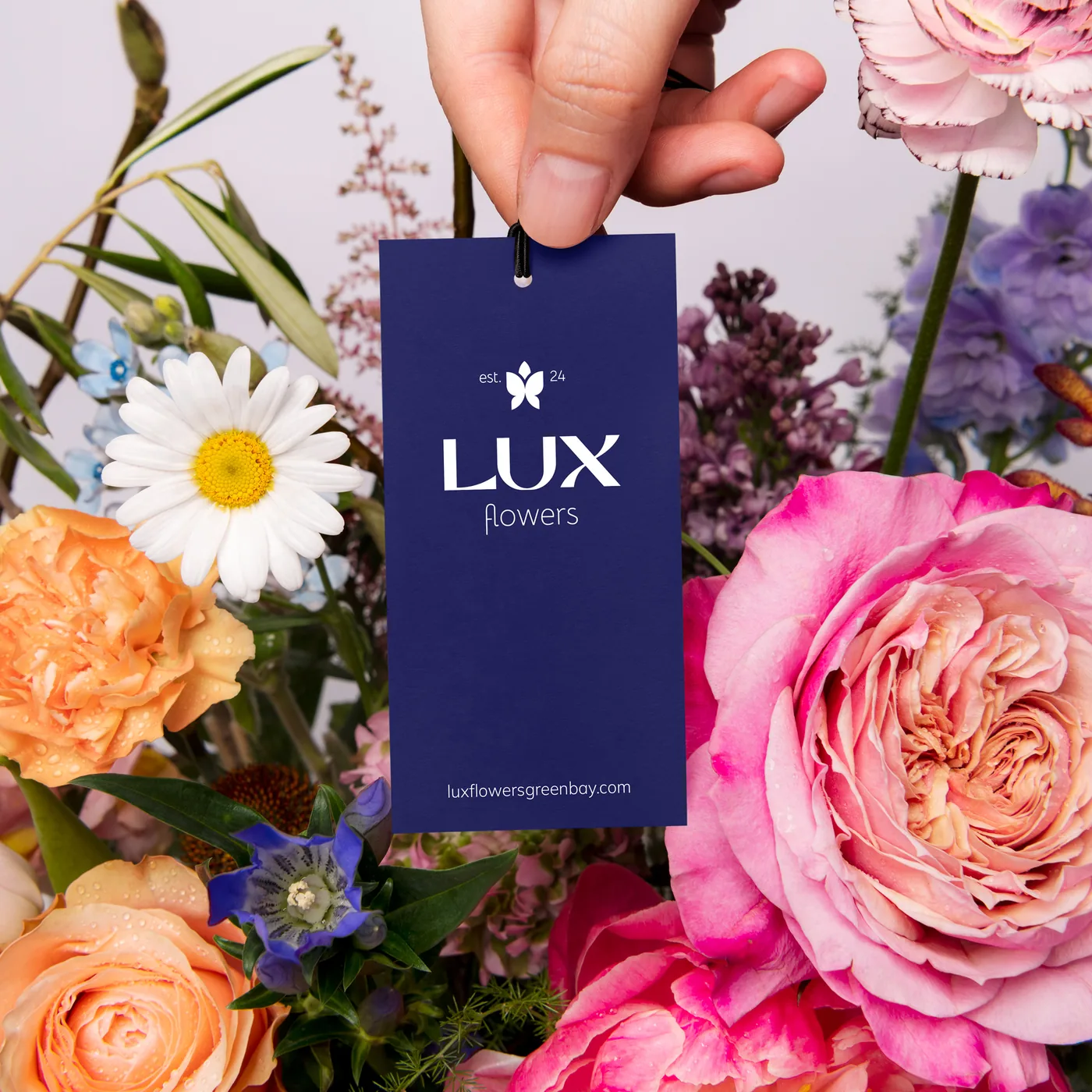 A navy Lux Flowers hangtag held in front of a colourful bouquet