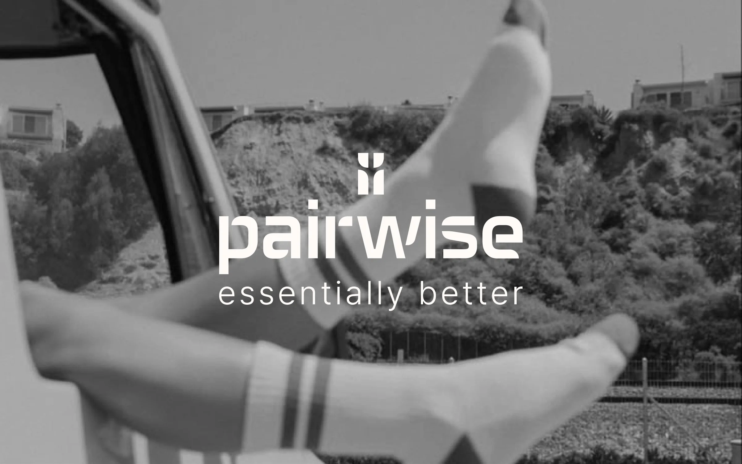 A pair of legs kicking up white ribbed socks against a black and white beach photo, with the Pairwise logo and the line &ldquo;essentially better&rdquo; over the image