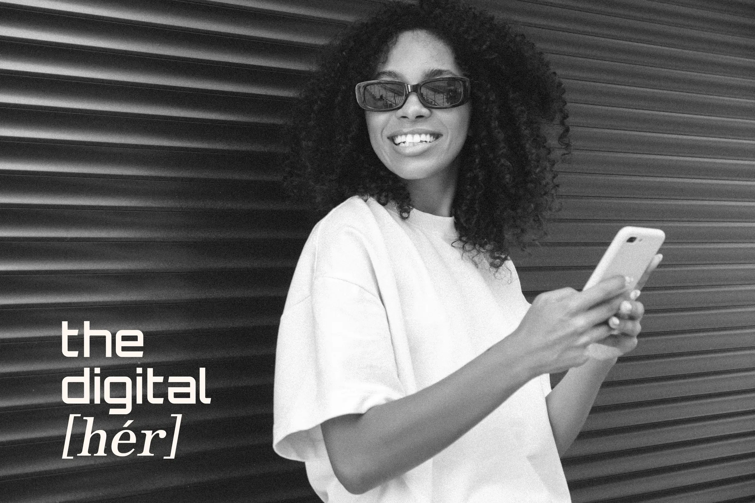 Vanessa holding her phone in front of a dark corrugated wall, the &ldquo;the digital [h&eacute;r]&rdquo; wordmark in ivory beside her