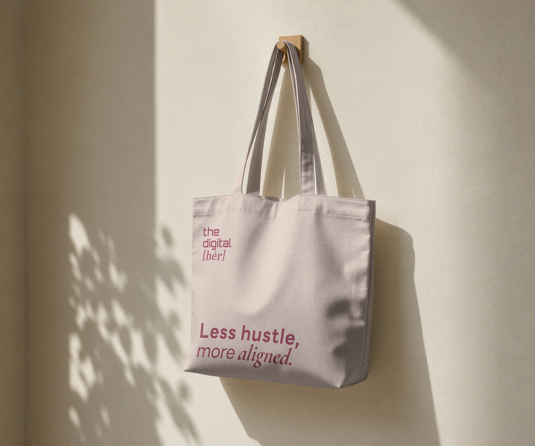 A tote bag in the brand&rsquo;s soft mauve, with the wordmark and the line &ldquo;Less hustle, more aligned.&rdquo;